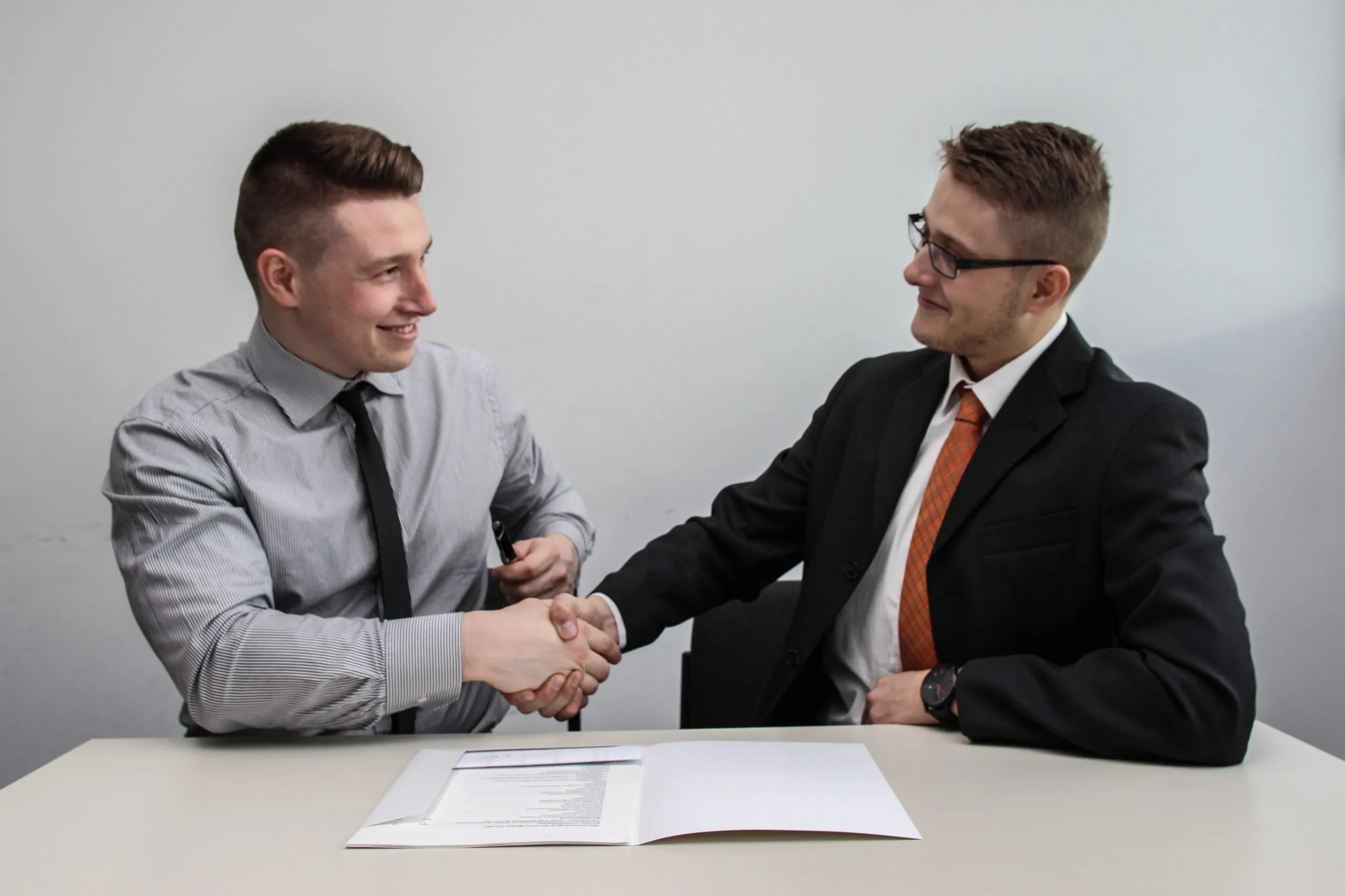 Photo of two men shaking hands over a proposal in formalwear